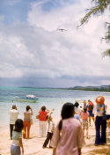 Wilcommen, No. 0168 Spectators on a Beach Photograph a Slim Aircraft Flying Above